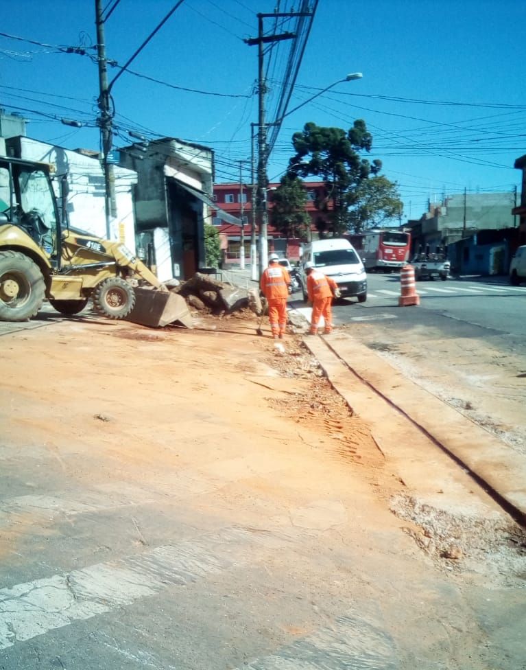 Funcionários varrendo a poeira da construção no meio-fio da avenida; à esquerda, um trator.